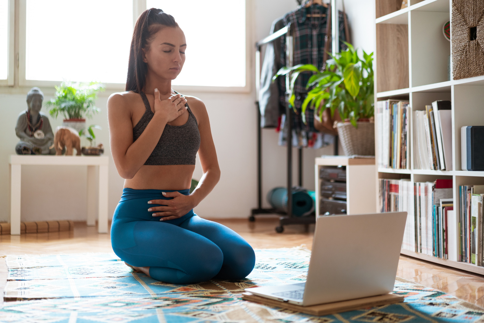 Young woman following online yoga class and doing her  breathing exercises at home
